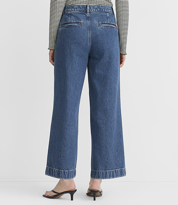 A person wearing wide-leg denim jeans and a striped shirt stands against a plain white background.