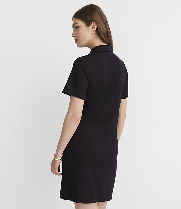 A woman in a black dress stands against a plain gray background.