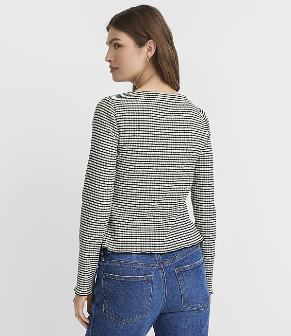 A woman in a checkered long-sleeved shirt and blue jeans stands against a plain white background.
