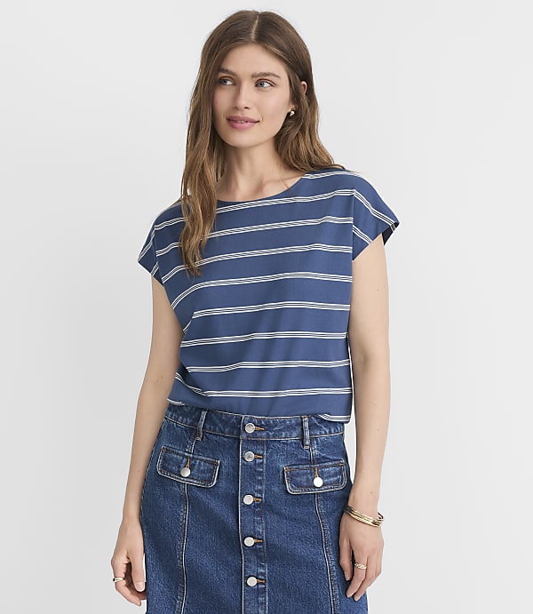 A woman in a blue and white striped t-shirt and denim skirt stands against a plain white background.
