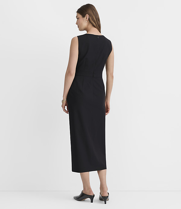A woman in a black dress stands against a plain white background.