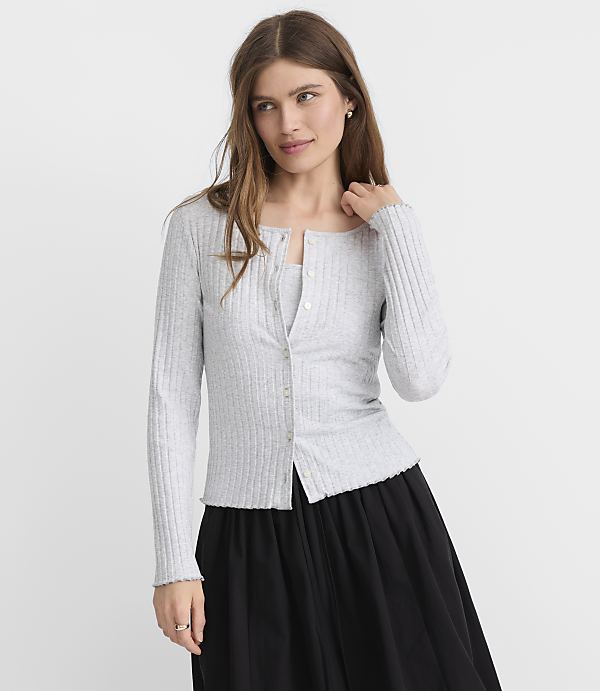 A woman in a light gray ribbed cardigan and black skirt stands against a plain gray background.