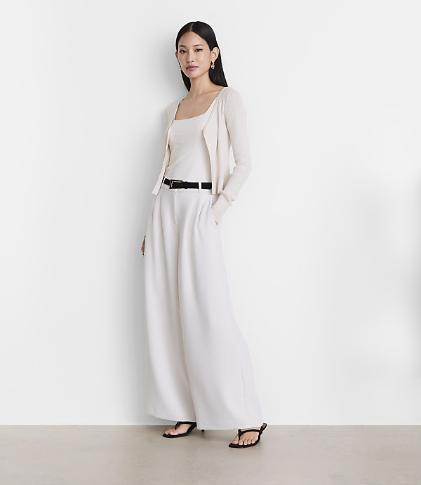 A woman in a cream-colored tank top, cardigan, and wide-leg pants stands against a plain white background.