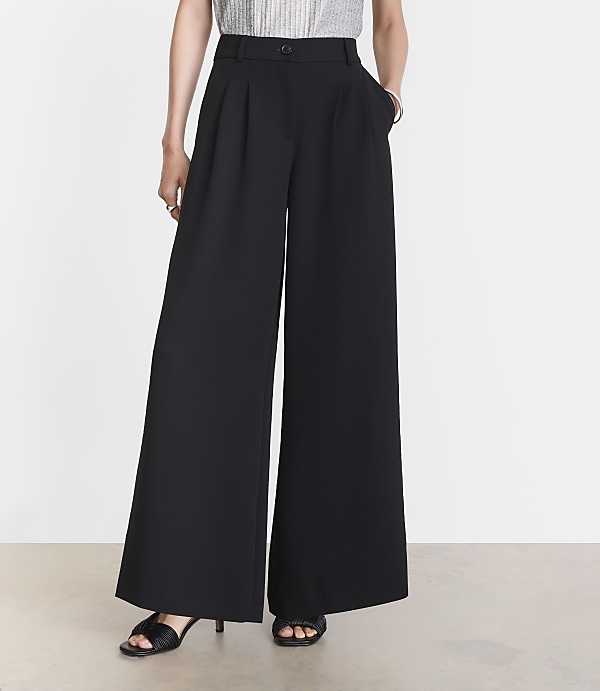 A person stands in black wide-leg pants and sandals against a plain white background.