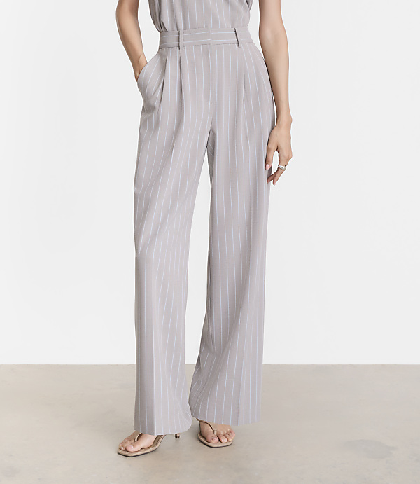 A person stands in light gray pinstripe wide-leg pants and sandals against a plain, light gray background.