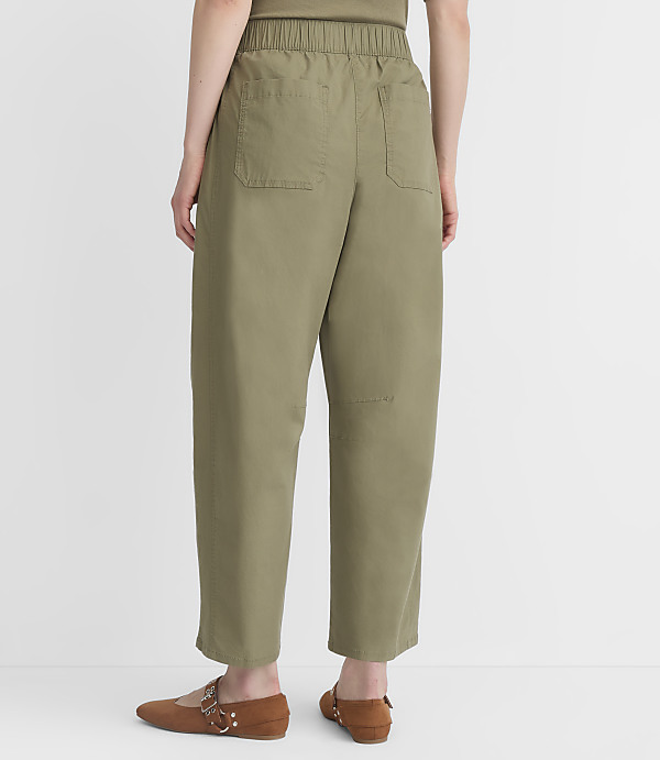 A person wearing olive green pants and brown flats stands against a plain white background.