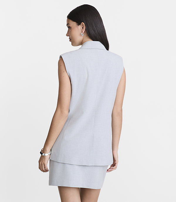 A woman in a light gray sleeveless blazer and skirt stands against a plain white background.
