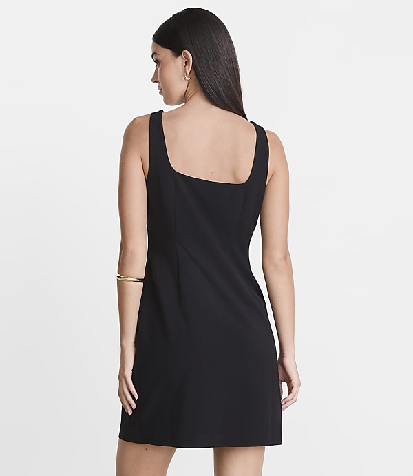 A woman in a black dress stands against a plain white background.