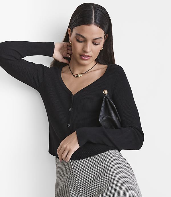 A woman in a black ribbed cardigan and patterned skirt poses against a plain white background.