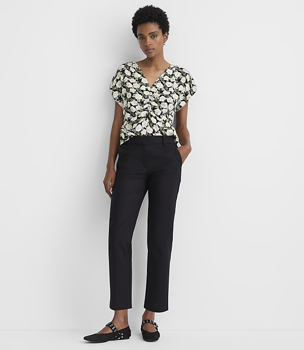 A woman in a floral top and black pants stands against a plain white background.