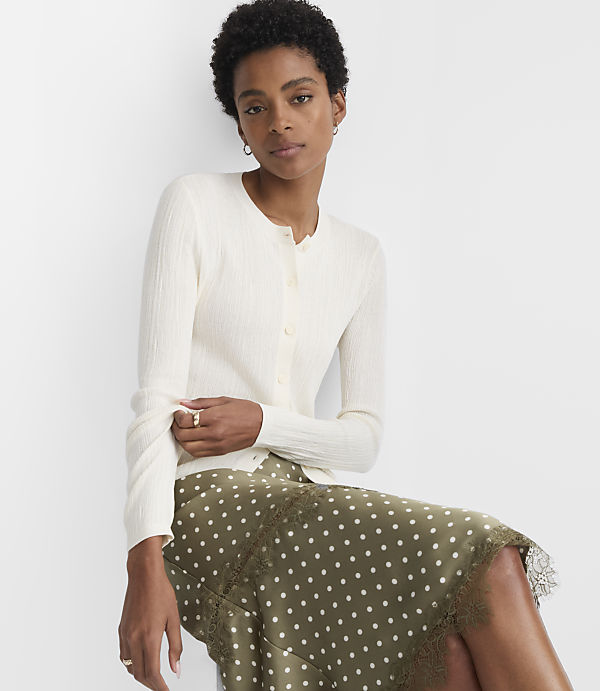 A woman in a cream cardigan and a polka dot skirt sits against a plain white background.