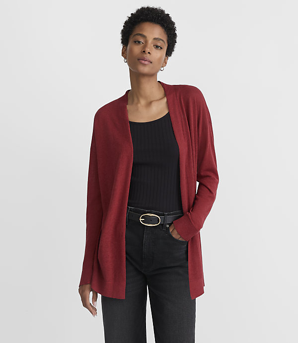 A woman in a red cardigan and black top stands against a plain gray background.