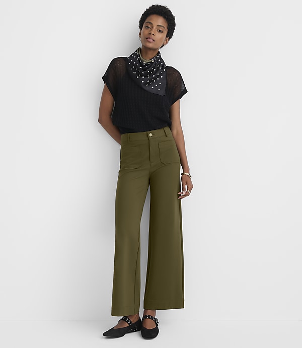 A woman in olive green wide-leg pants and a black top stands against a plain white background.