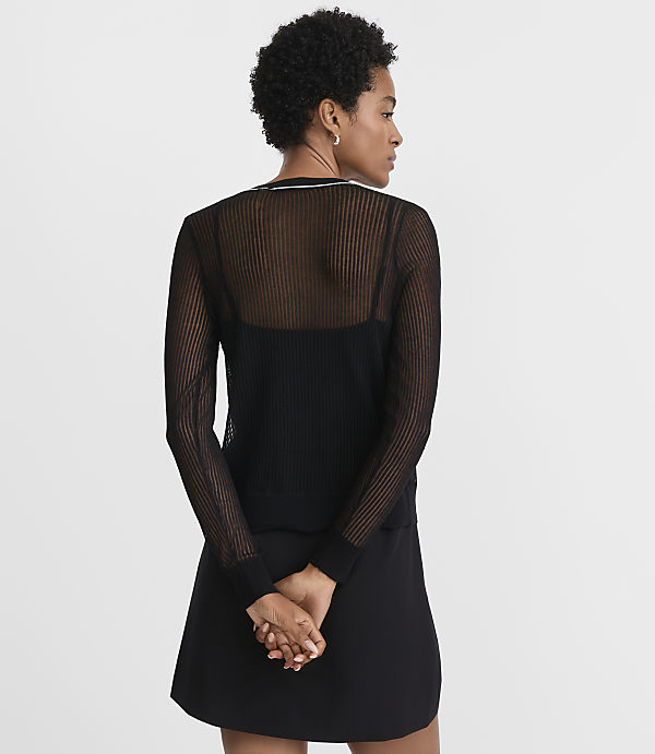 A woman in a sheer black top and black skirt stands with her back to the camera against a plain white background.