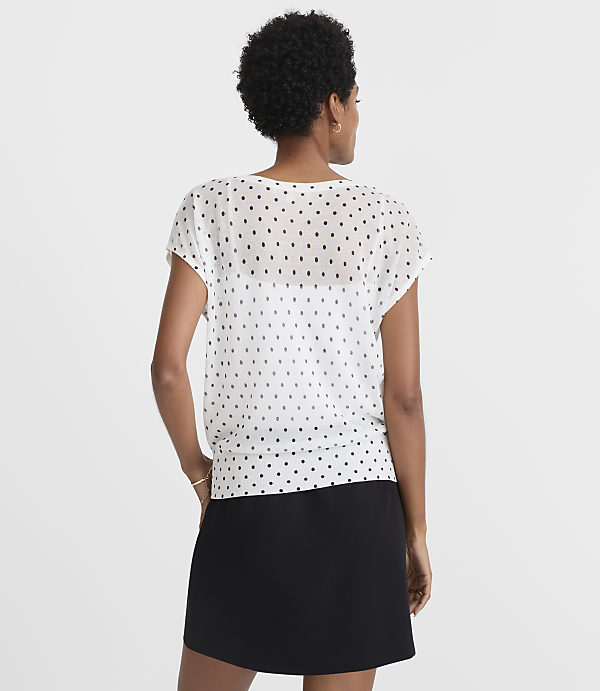 A woman in a white polka-dot blouse and black skirt stands against a plain white background.