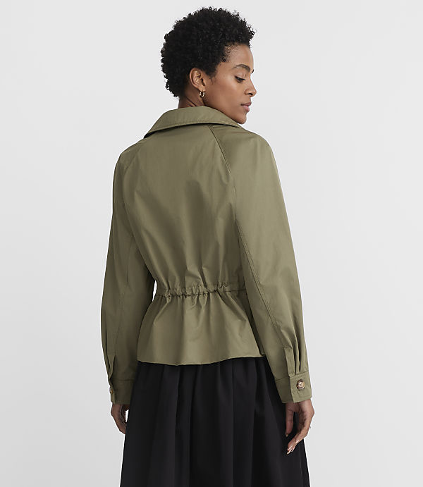 A woman in a green jacket and black skirt stands against a plain white background.