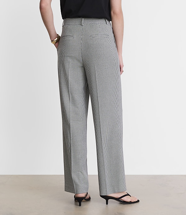 A person wearing black and white checkered pants and black kitten heels stands against a plain white background.