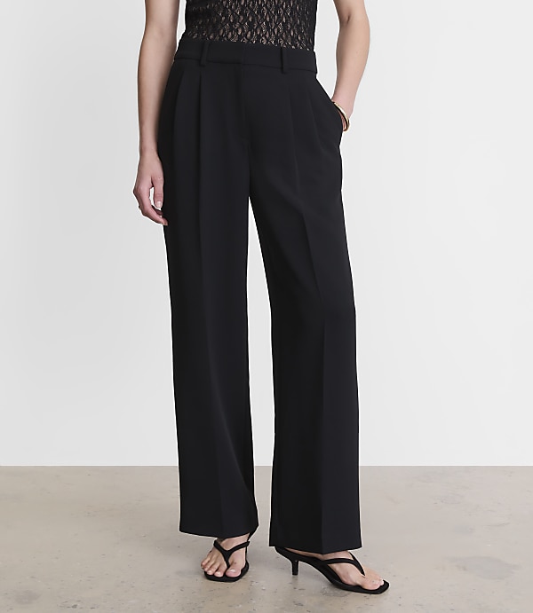 A person stands in black wide-leg trousers and sandals against a plain white background.
