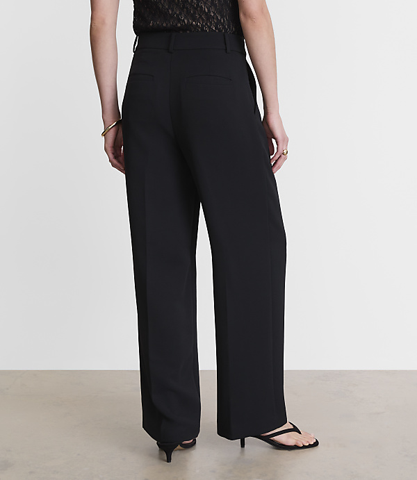 A person wearing black wide-leg pants and a patterned top stands against a plain, light-colored background.