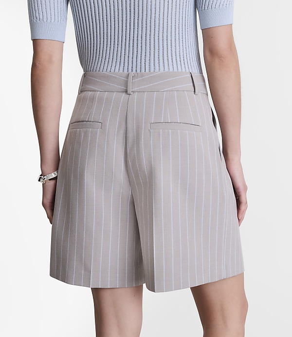 A person wearing pinstripe shorts and a light blue top stands against a plain white background.