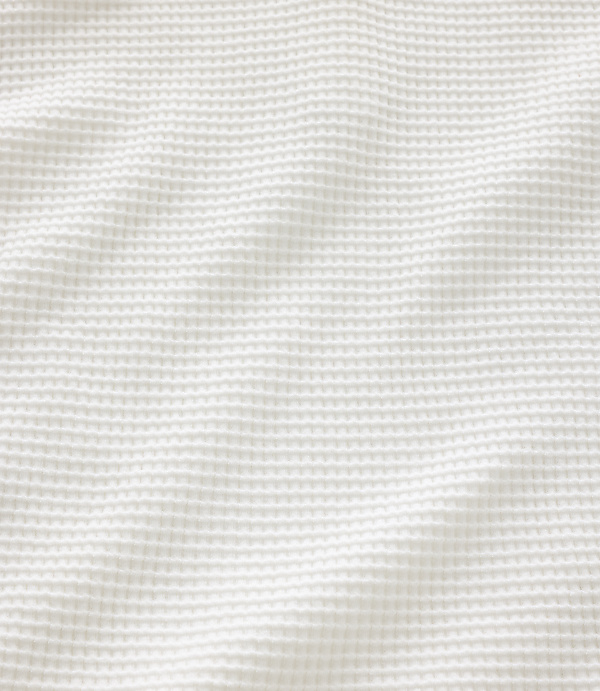 A white waffle-knit fabric with soft folds fills the frame, creating a textured and gentle background.