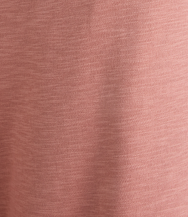 A close-up of a textured, dusty rose fabric fills the frame, with subtle variations in shade creating a soft, mottled background.
