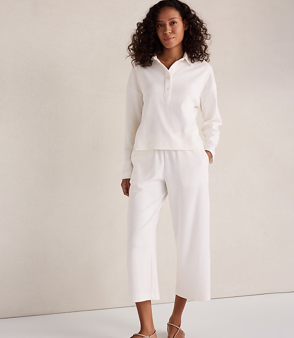 A woman in a white loungewear set stands against a textured, light-colored wall.