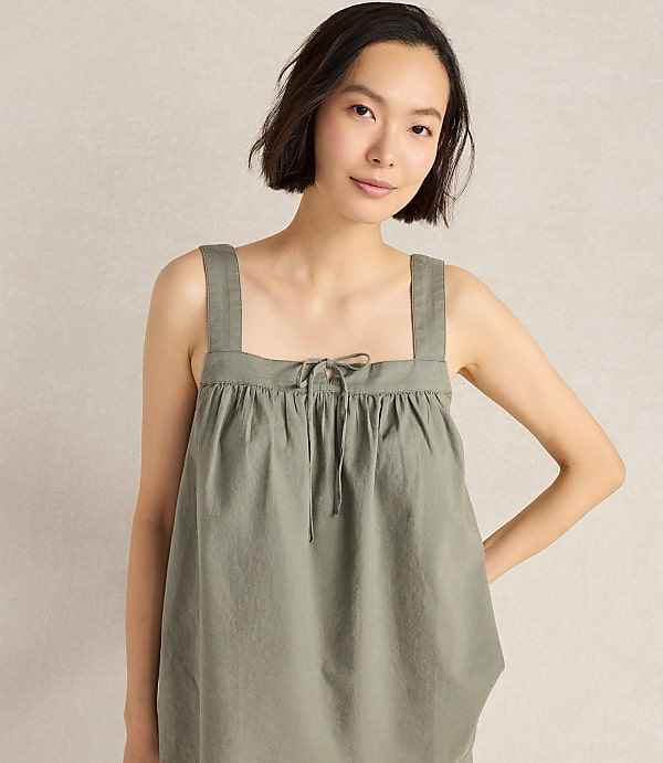 A young woman in a green top stands against a plain, light-colored background.