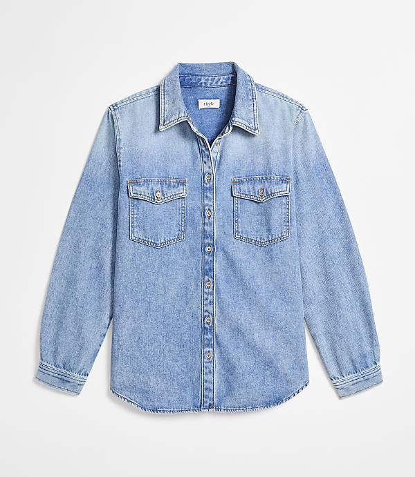 A light blue denim shirt with two chest pockets is laid flat against a plain white background.