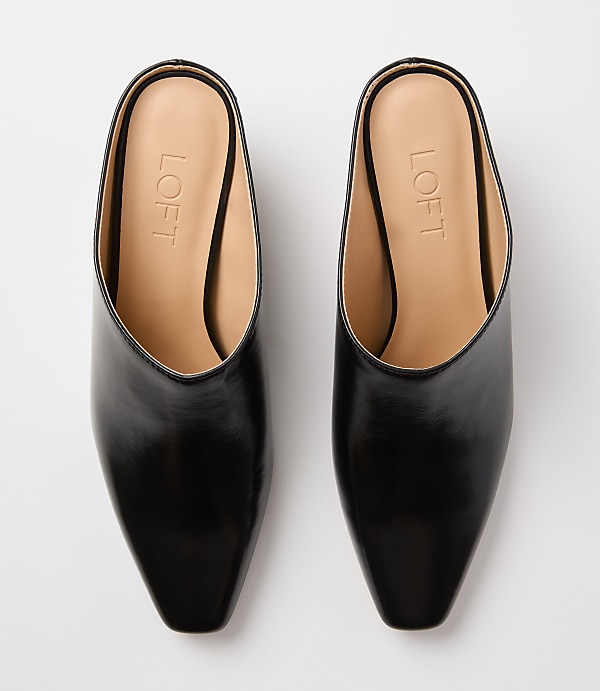 A pair of black leather pointed-toe mules with "LOFT" branding on the insoles rests on a plain white background.