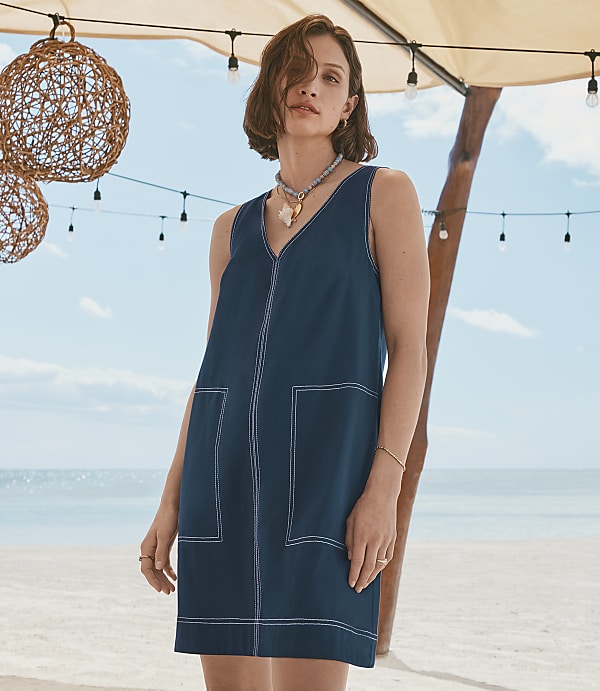 A woman in a dark blue dress stands on a beach with decorative lights and spheres hanging overhead.