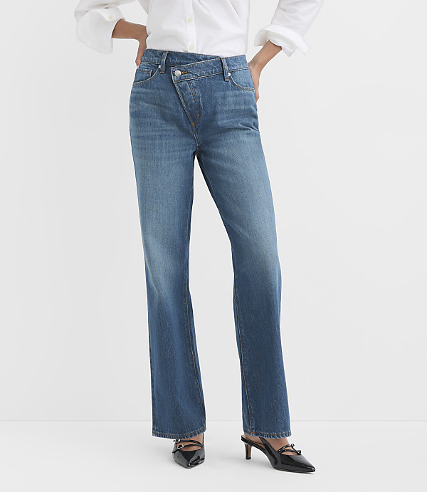 A person stands in blue denim jeans with a white shirt and black heels against a plain white background.