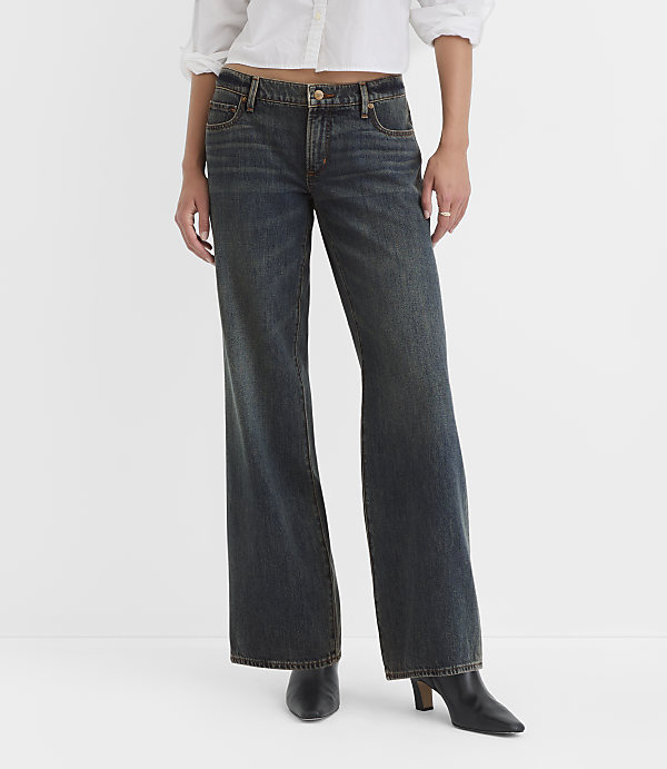 A person wearing dark wash wide-leg jeans and black heeled boots stands against a plain white background.