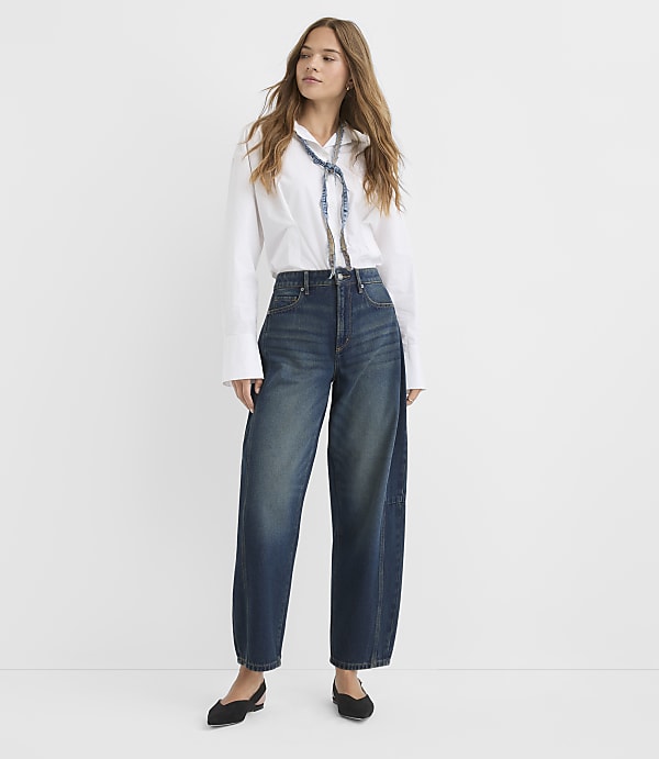 A woman in a white shirt and wide-leg jeans stands against a plain white background.