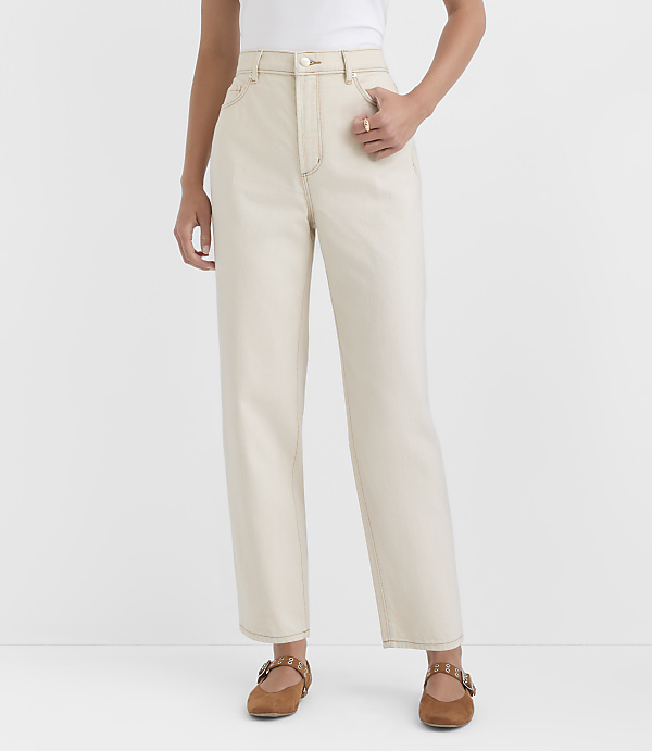 A person stands in the foreground wearing cream-colored jeans and brown flats against a plain white background.