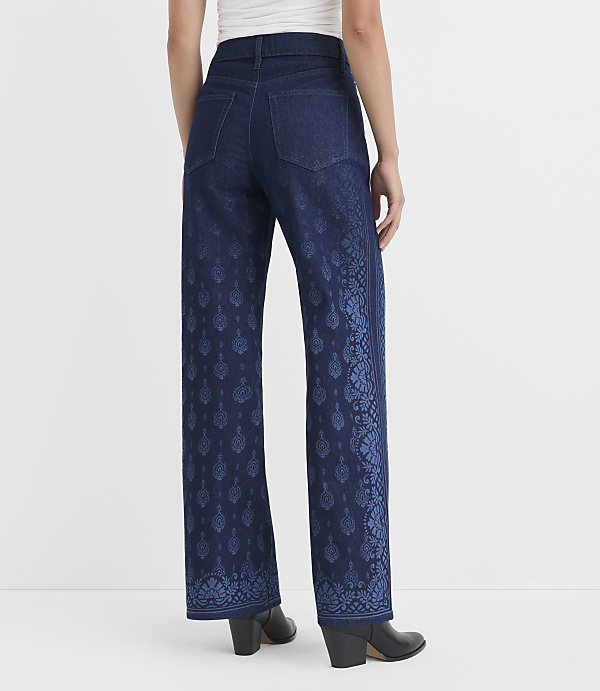 A person wearing dark wash wide-leg jeans with a blue floral pattern on the lower legs stands against a plain white background.