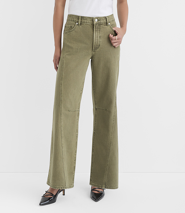 A person stands in the foreground wearing olive green wide-leg jeans and black heels against a plain white background.