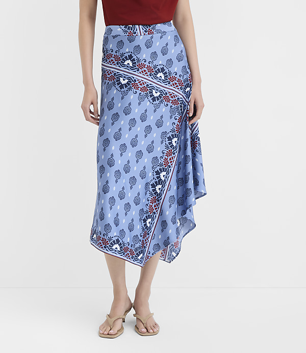 A woman in a patterned blue skirt and sandals stands against a plain white background.