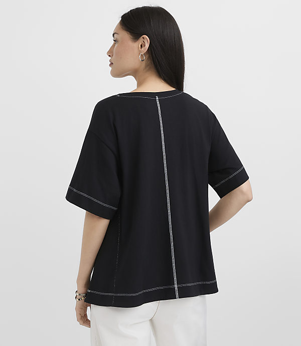 A woman in a black t-shirt with white stitching stands against a plain white background.