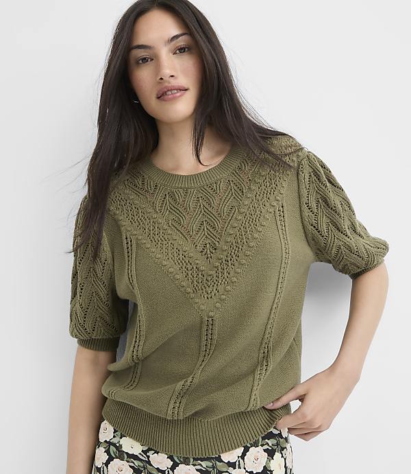 A woman in a green, textured sweater stands against a plain white background.