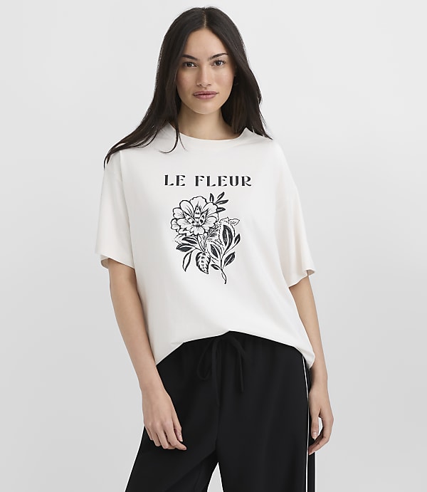 A woman in a white t-shirt with a floral design stands against a plain gray background.