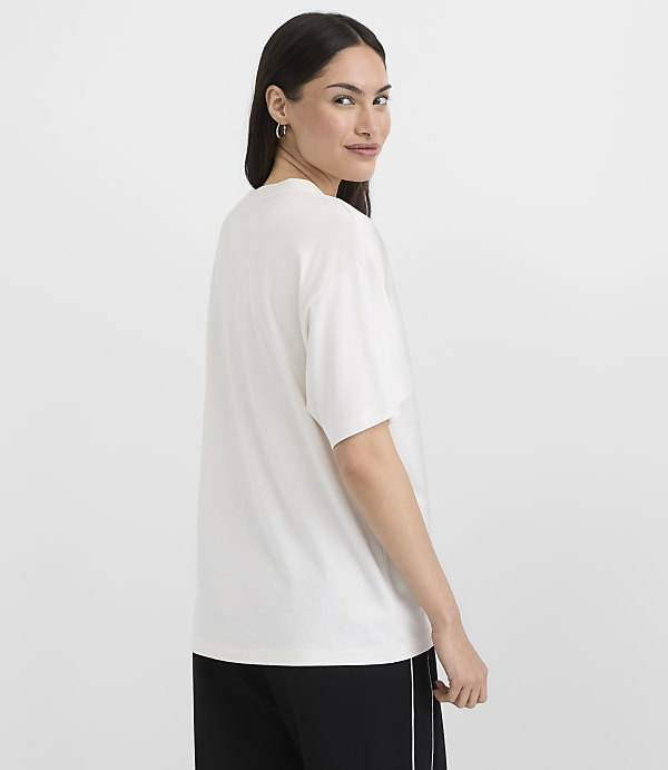 A woman in a white t-shirt and black pants stands against a plain white background.