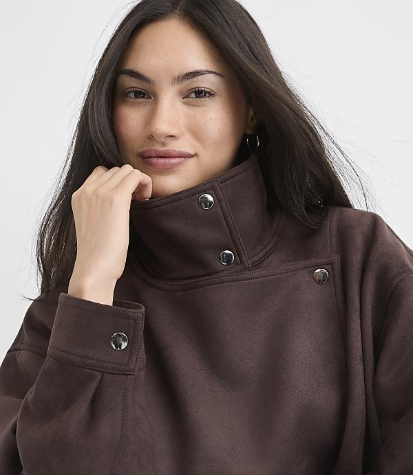 A woman in a brown mock-neck sweatshirt with silver snaps poses against a plain white background.