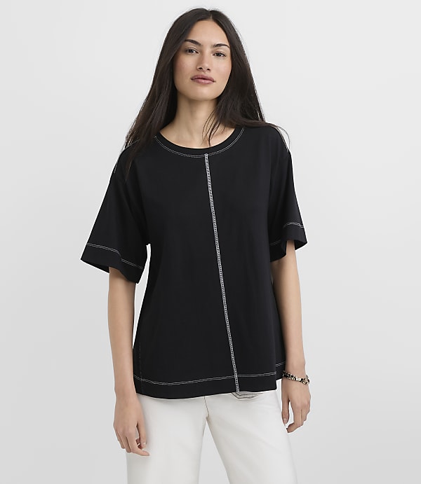 A woman in a black t-shirt with white stitching stands against a plain white background.