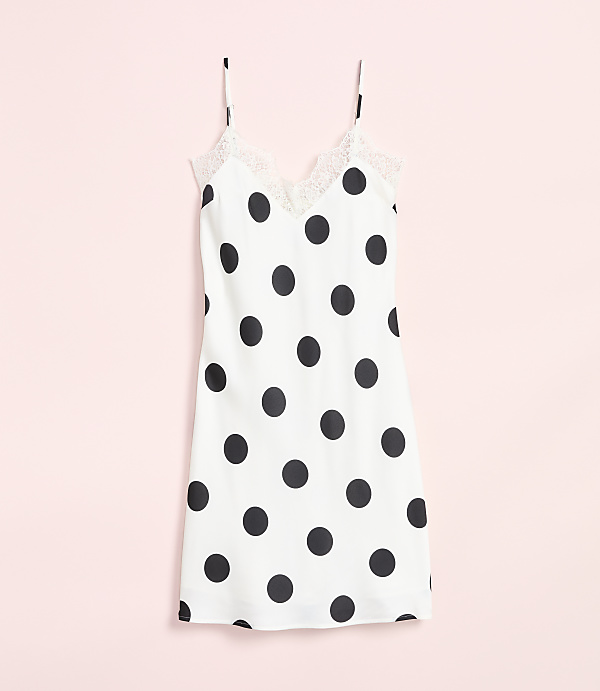 A white polka dot slip dress with lace trim hangs against a soft pink background.