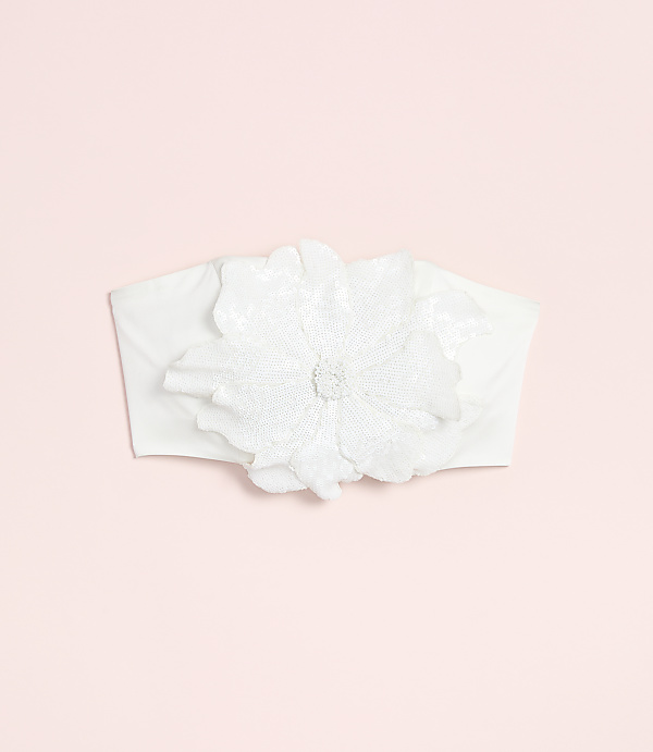A white fabric headband with a large, ornate flower adorns a soft pink background.