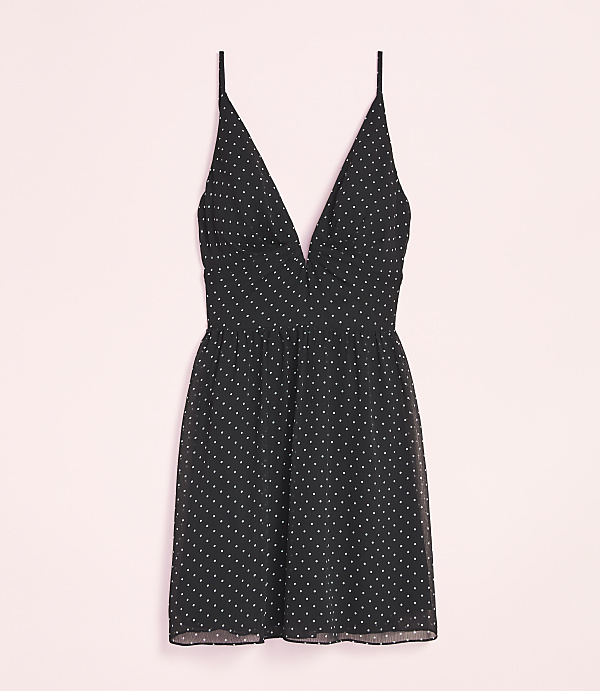 A black polka dot mini dress with thin straps is laid out against a soft pink background.