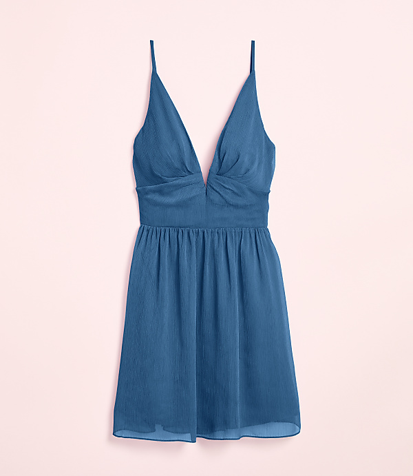 A teal slip dress with a deep V-neckline and spaghetti straps rests against a soft pink background.