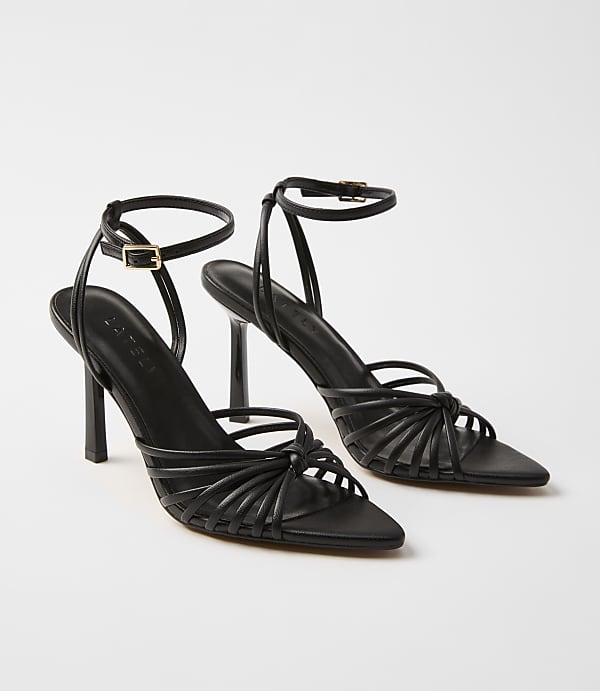 A pair of black strappy high-heeled sandals with ankle straps are displayed against a plain white background.