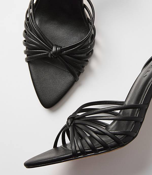 Black strappy heels with knotted details are arranged on a plain white background.